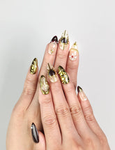 Model wearing Regal Radiance handmade Singapore press on nails in deep burgundy with gold accents and pearl embellishments